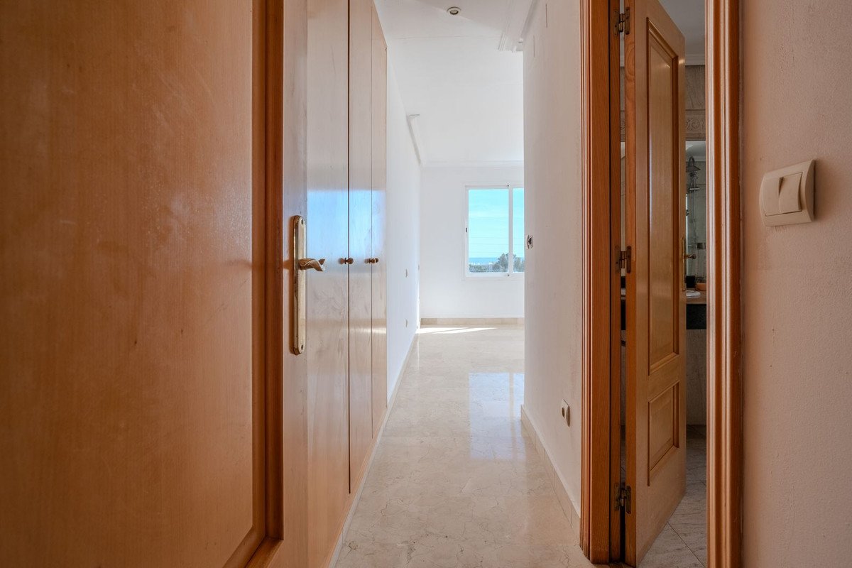 A bright hallway with wooden closet doors, marble flooring, and a window showing a sea view.