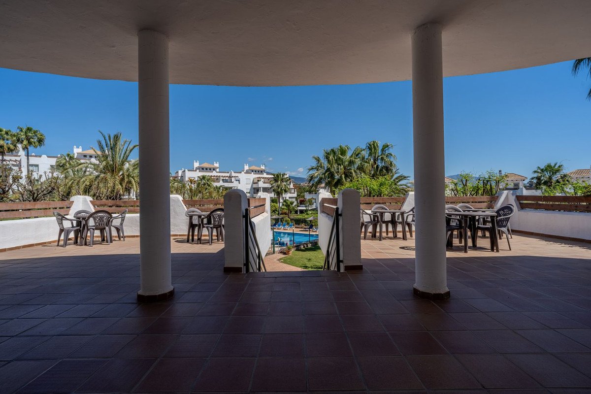 Outdoor terrace with tables, chairs, and pool view under sunny sky