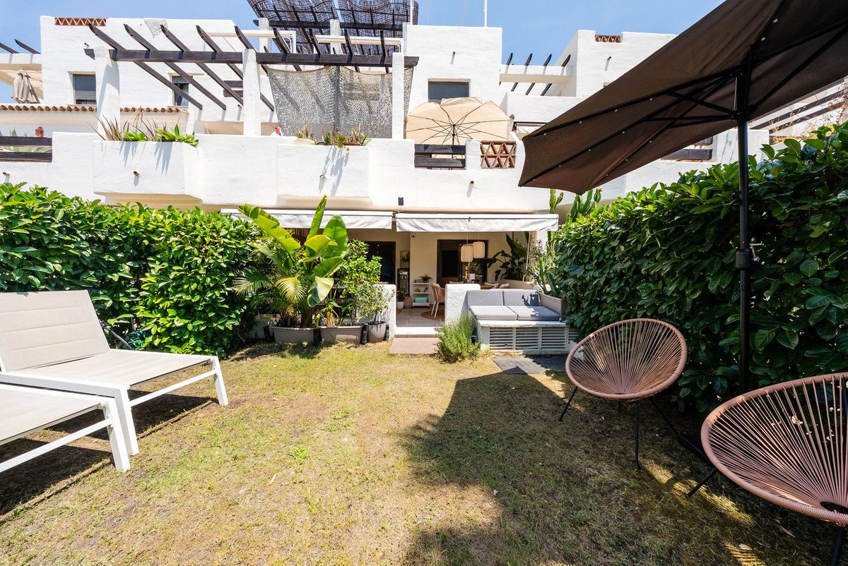 A sunny garden with lounge chairs, outdoor sofa, and a shaded patio area in front of a white building.