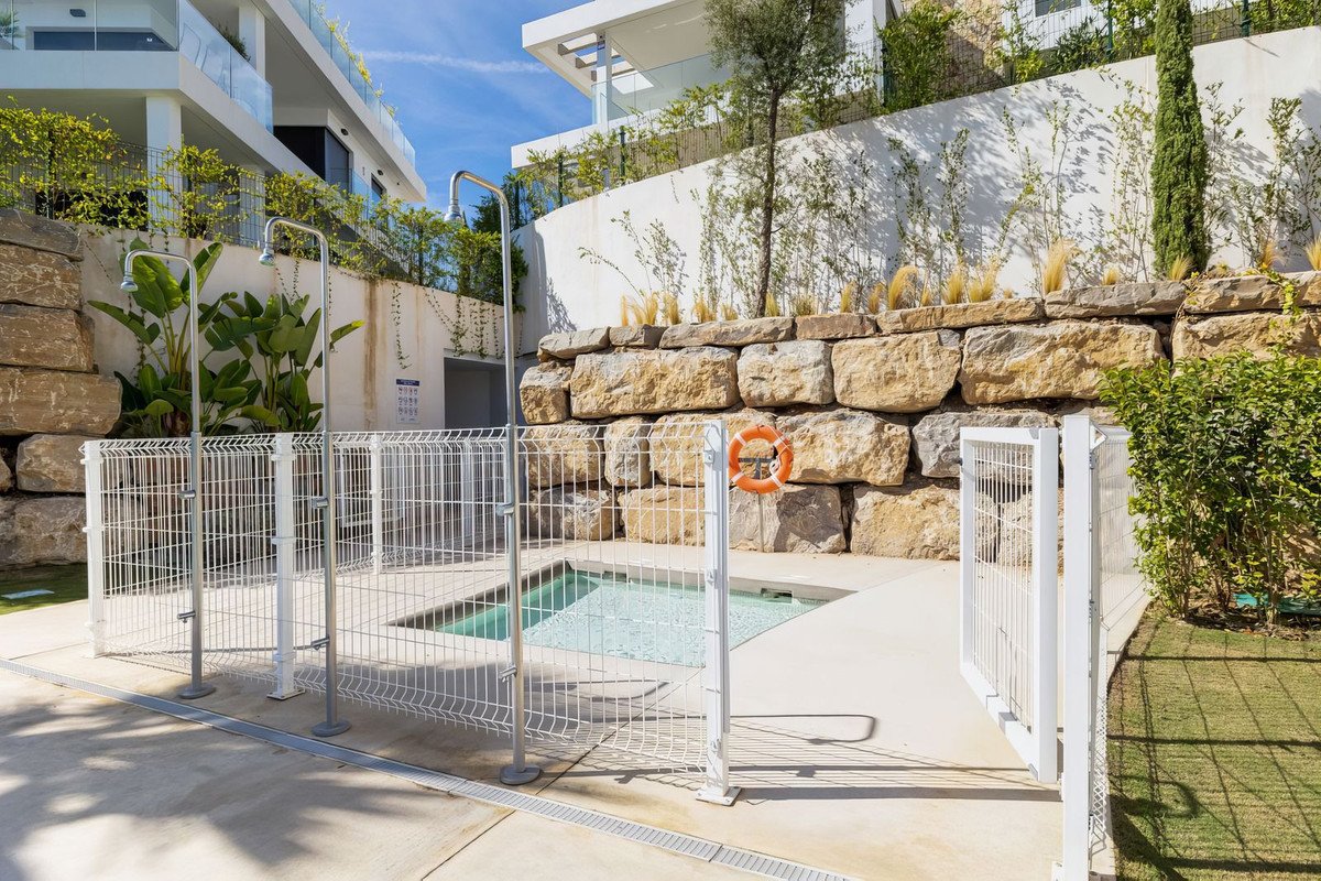 An outdoor area with a small pool, two showers, and a safety ring mounted on a stone wall.