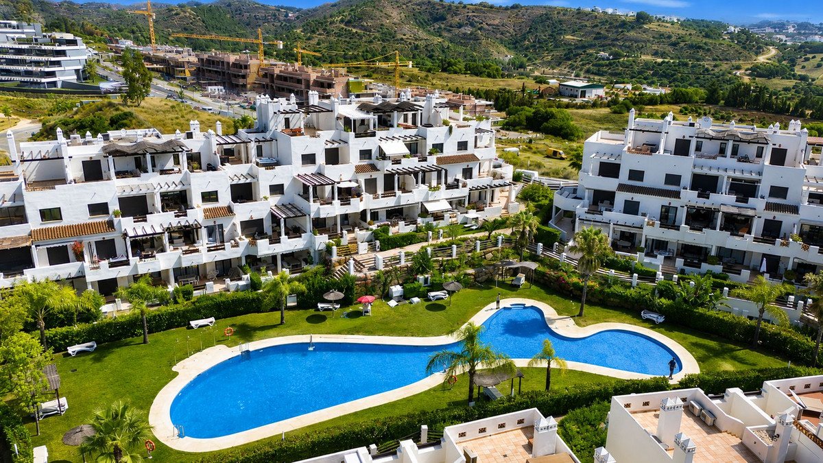Aerial view of modern apartment complex with swimming pool and lush gardens, offering sea views and balconies.