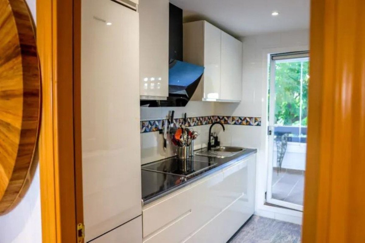 A modern, compact kitchen with white cabinets, a black countertop, and a balcony with a green outdoor view visible view.