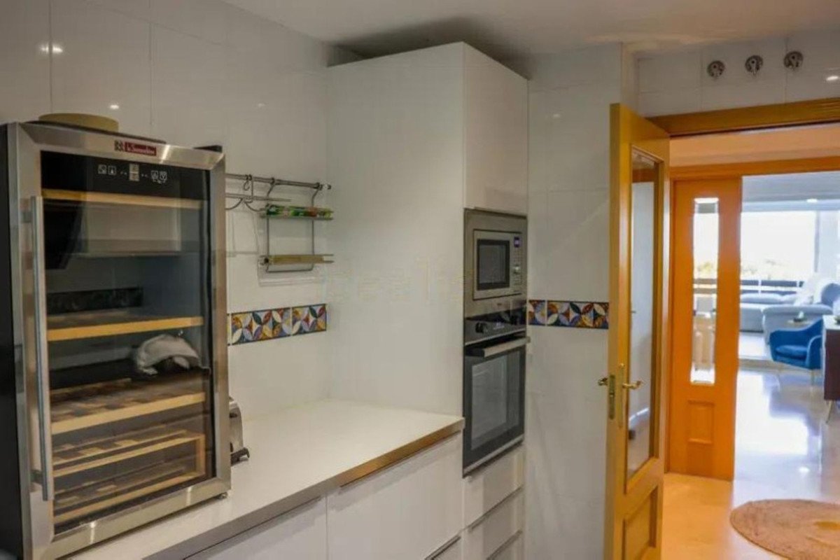 Modern kitchen featuring a wine cooler, oven, microwave, and decorative tile backsplash, with a glimpse of a living area through an orange door.