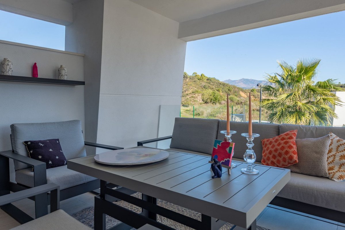 Outdoor patio seating area with a table and sofa, featuring a view of rolling hills and mountains with palm trees.
