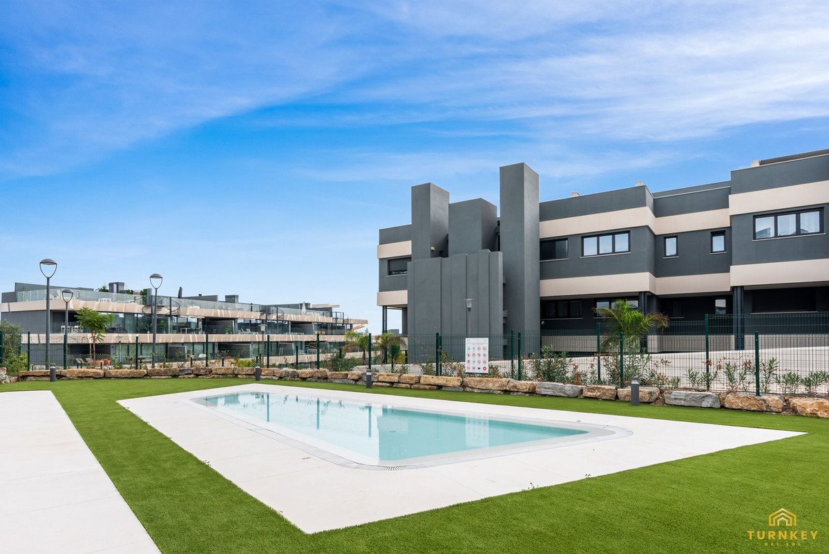 Modern apartment complex with a shared swimming pool and neat green lawn under a clear blue sky.