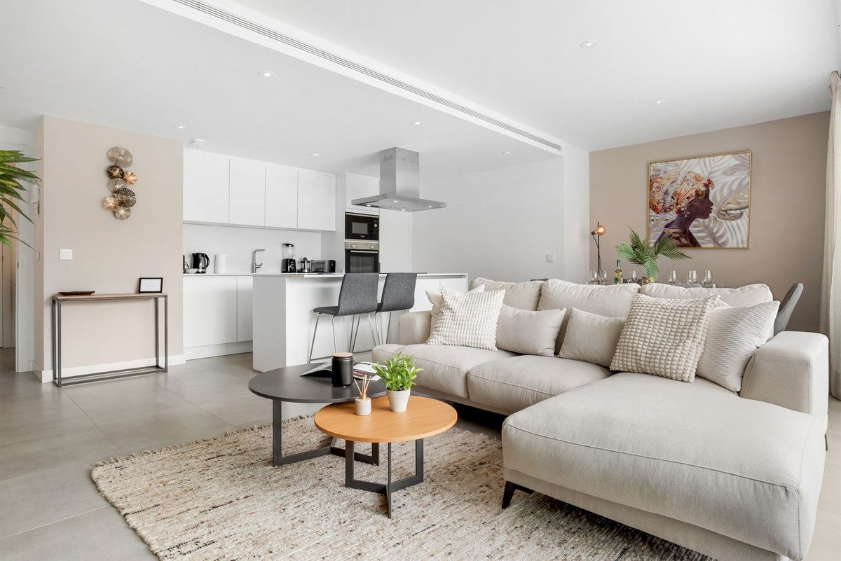A spacious open-plan living room and modern kitchen with a sectional sofa, coffee tables, and breakfast bar.