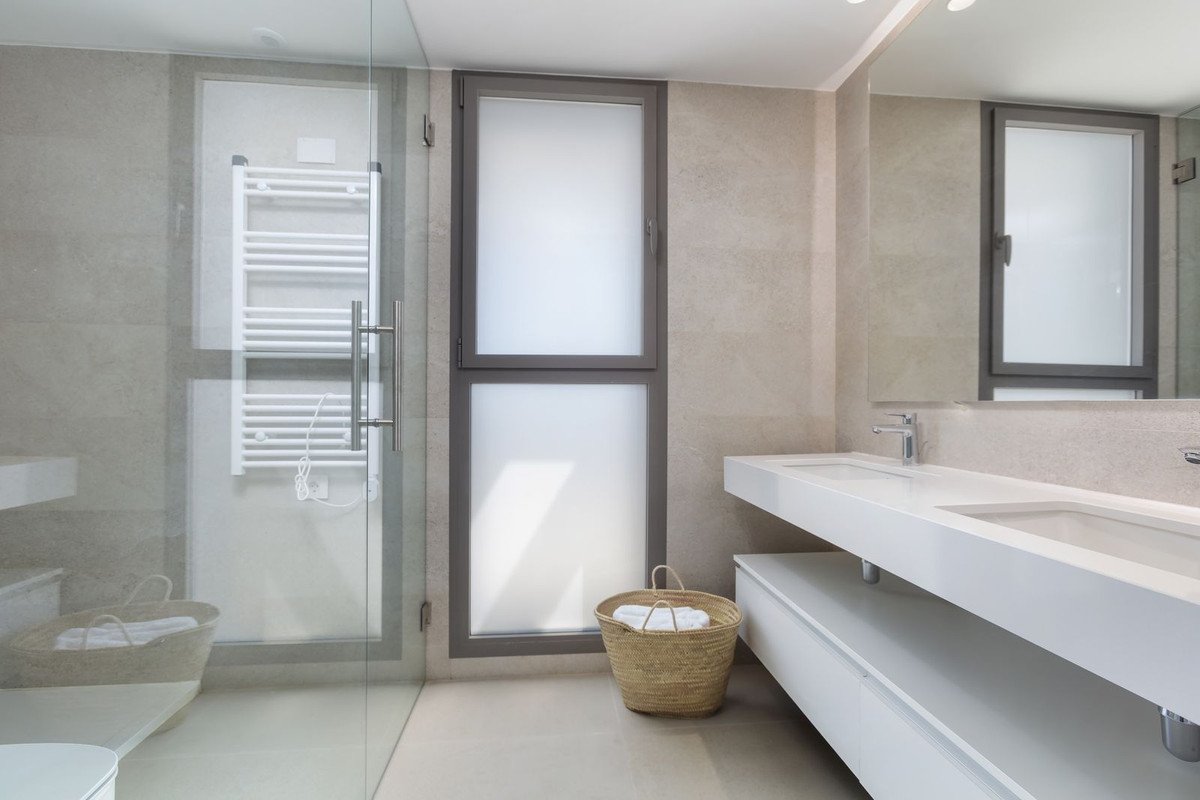 Modern bathroom with double sink, glass shower, and wicker basket.