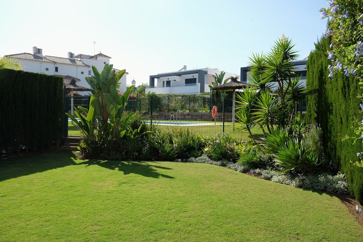 Well-kept garden with lush greenery, a swimming pool, and modern houses in the background on a sunny day.