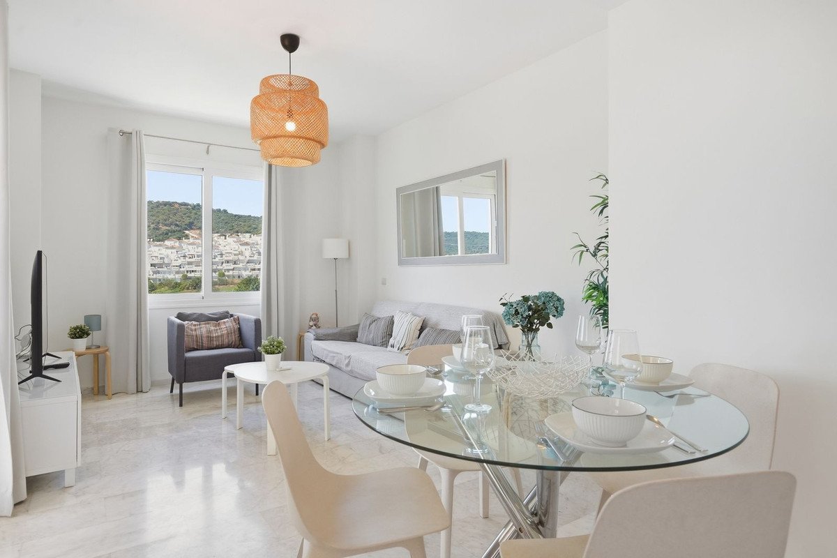 Bright living and dining area with a glass table set for a meal and a sofa, featuring a scenic town and mountain view from the window.