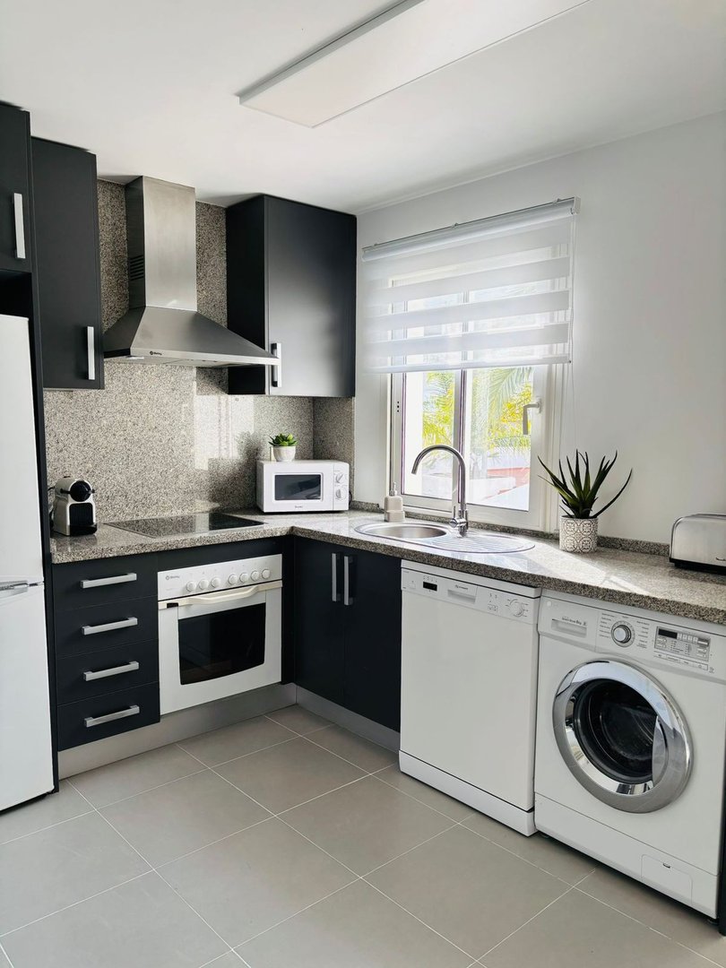 A modern kitchen with dark cabinets, granite countertops, oven, microwave, dishwasher, and washing machine visible.