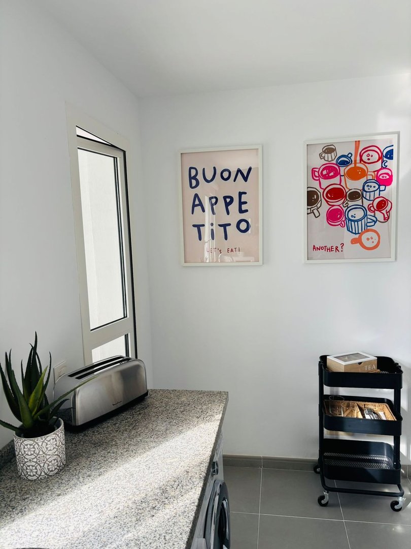 A modern kitchen counter with a toaster, decorative art on the wall, and a rolling cart with tea items.