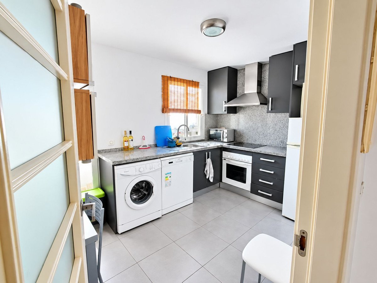 A modern kitchen featuring dark cabinets, a stainless steel hood, oven, microwave, dishwasher, and washing machine.