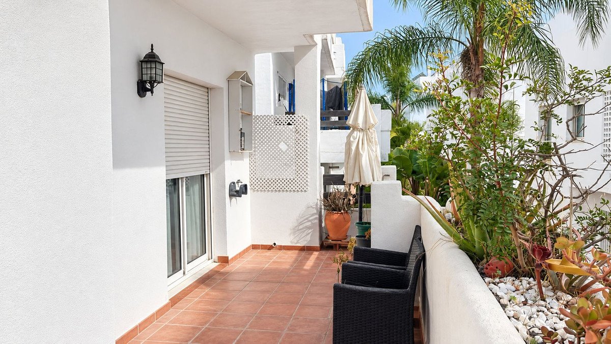 Balcony with black patio furniture, plants, and white building exterior.