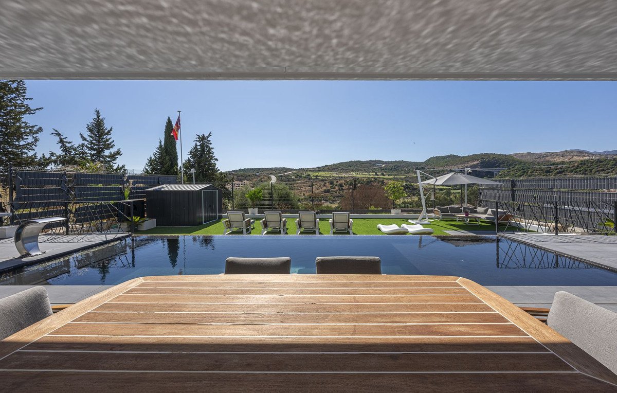 Infinity pool and patio with lounge chairs and umbrella overlooking rolling hills and countryside under a clear blue sky.