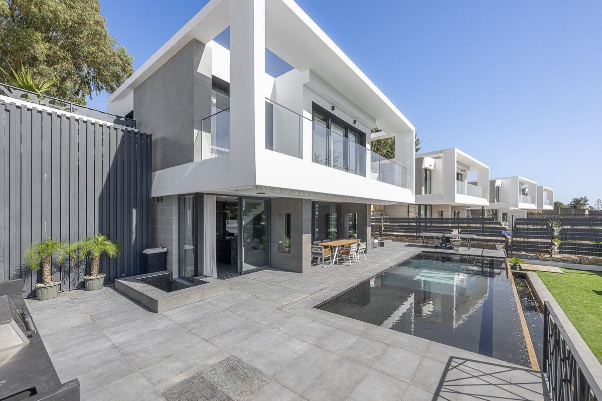 Modern white and grey house with a swimming pool, outdoor dining area, and a lush green lawn on a sunny day.