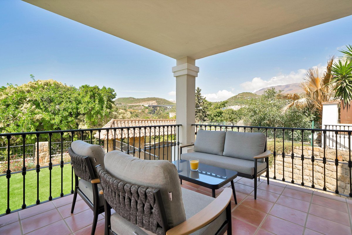Comfortable outdoor seating area on a terrace with a beautiful view of green hills and mountains under a clear blue sky.