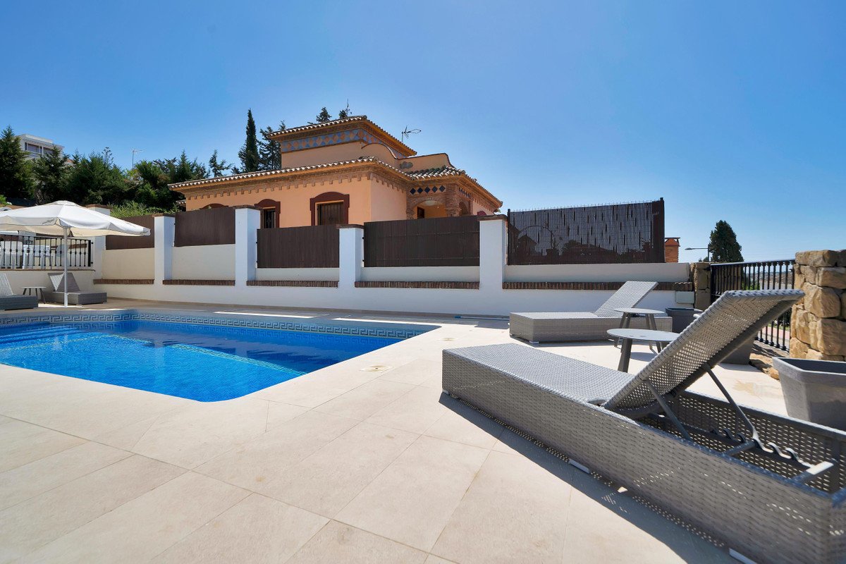 A refreshing swimming pool with lounge chairs and umbrellas, overlooking a property on a sunny day.