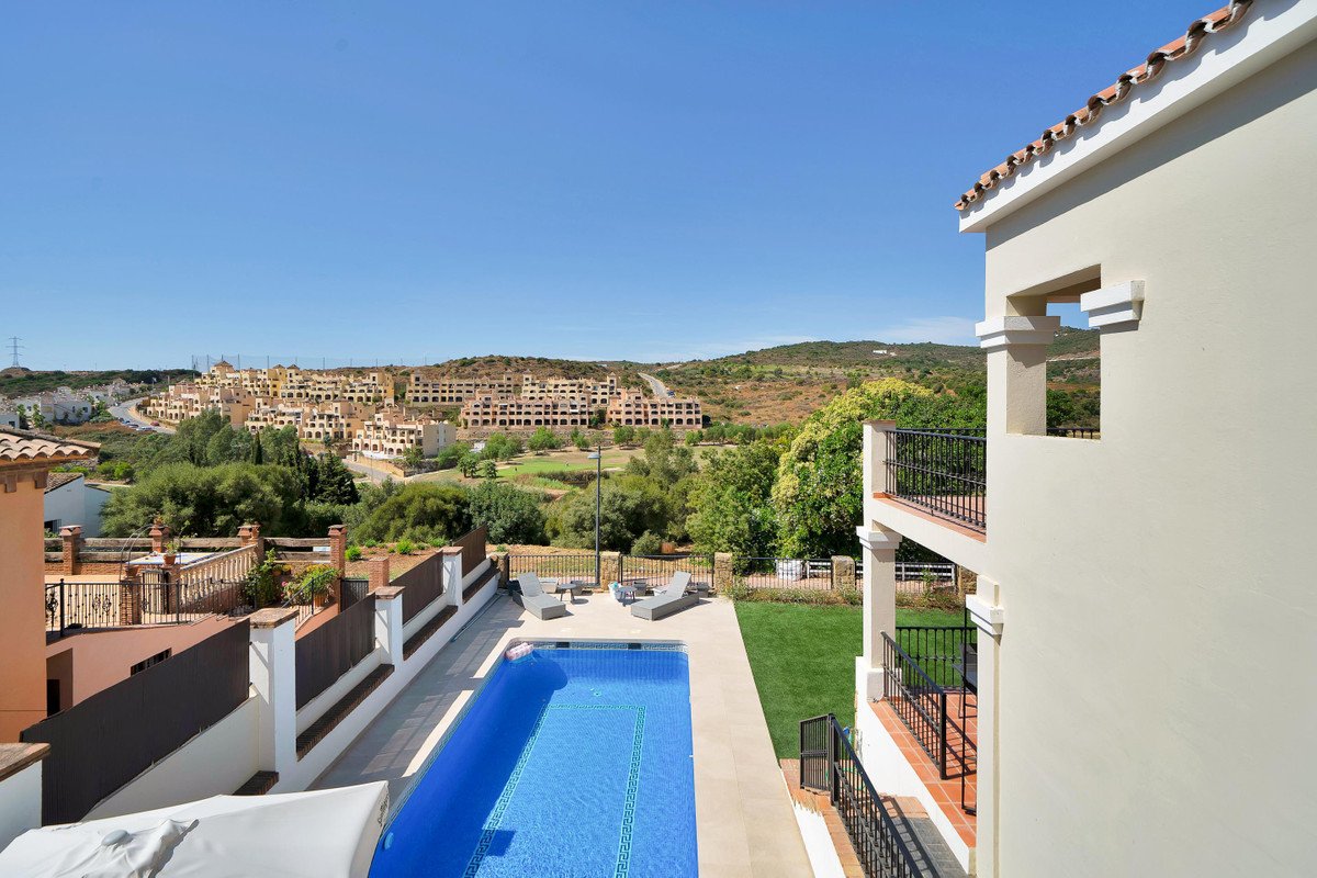 View of a swimming pool, terrace, and distant hills with residential buildings and lush greenery.