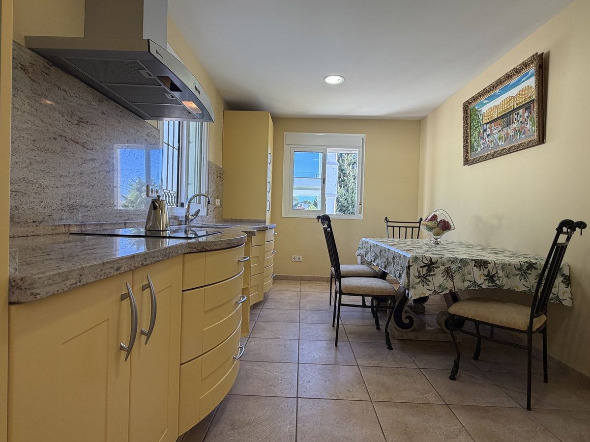 Modern kitchen with dining table and chairs, featuring a sea view from the window and light yellow cabinets.