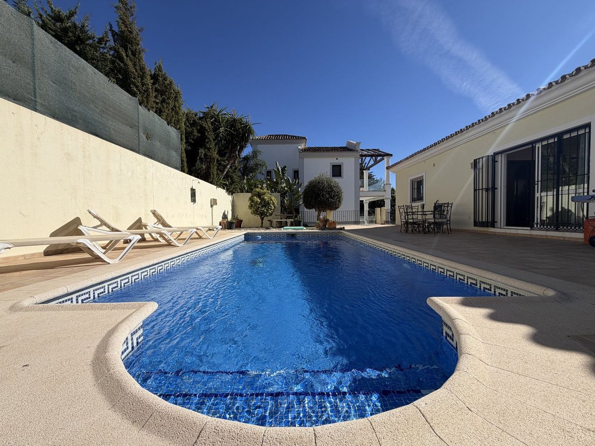 A beautiful private swimming pool with sun loungers and a patio area, surrounded by trees and a villa.
