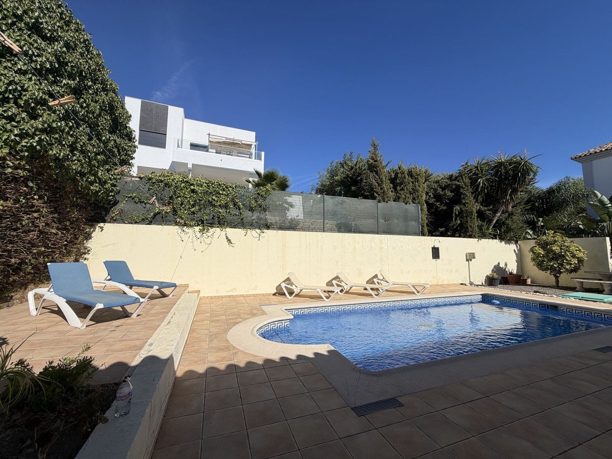 Outdoor swimming pool with blue tiled edge, sun loungers, and a modern villa in the background on a sunny day.