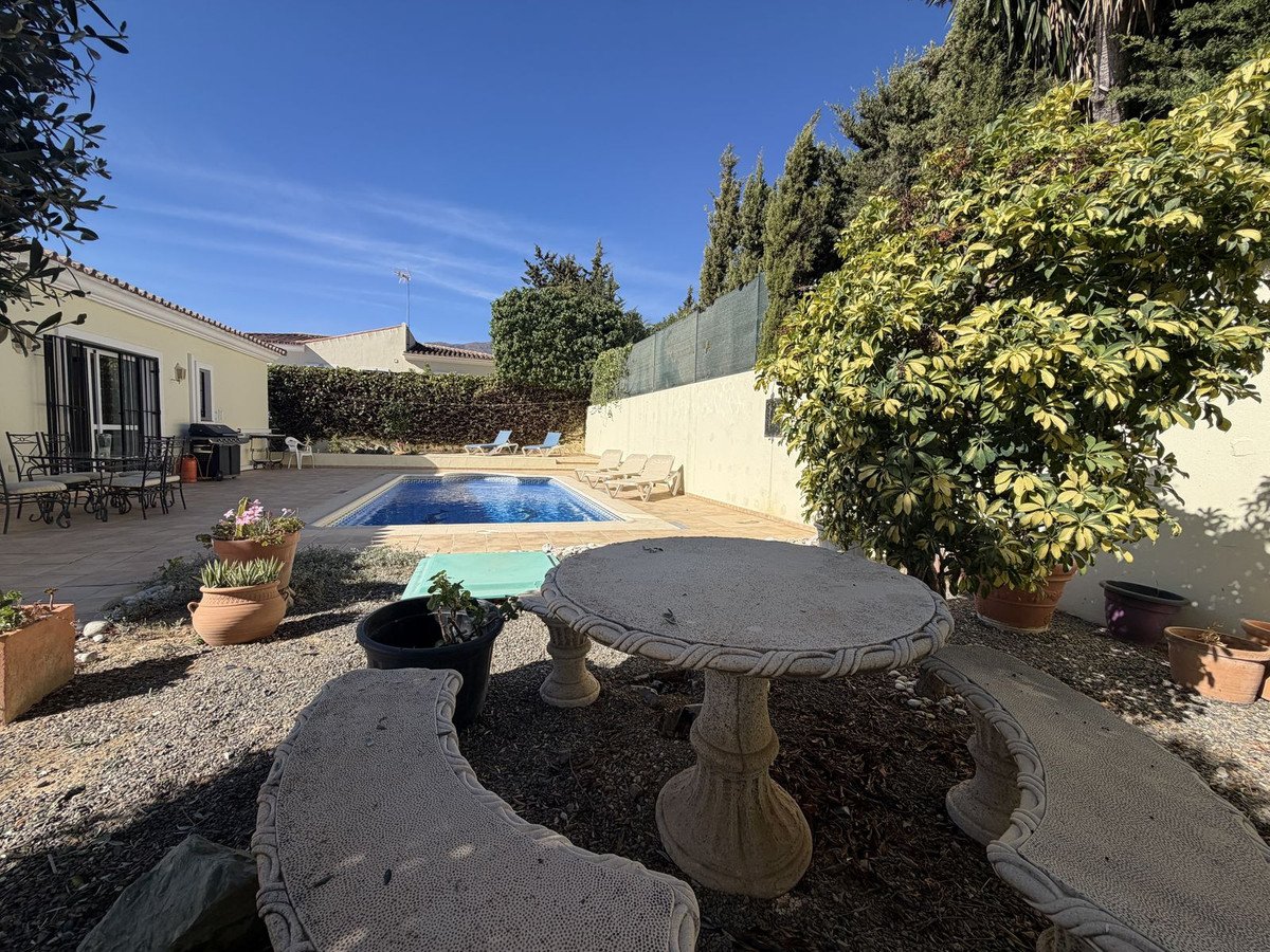 Exterior view of a house with a swimming pool, patio furniture, and lush greenery under a clear blue sky.
