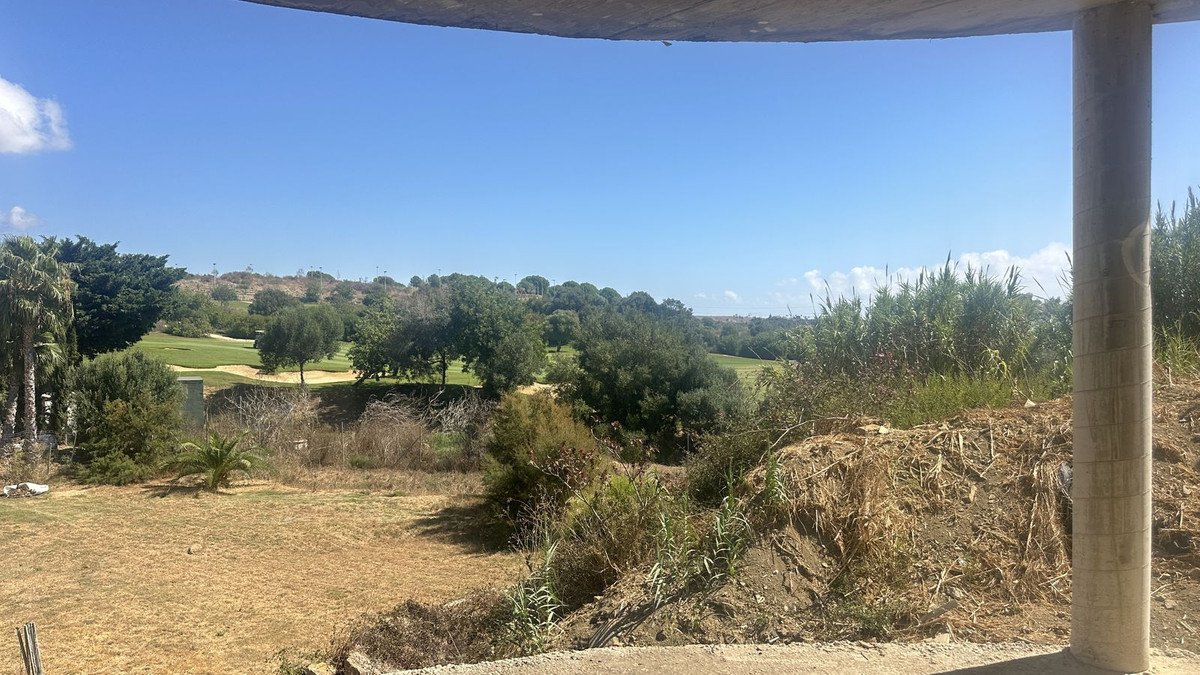 View from a balcony overlooking a lush green golf course with trees and clear blue sky on a sunny day.