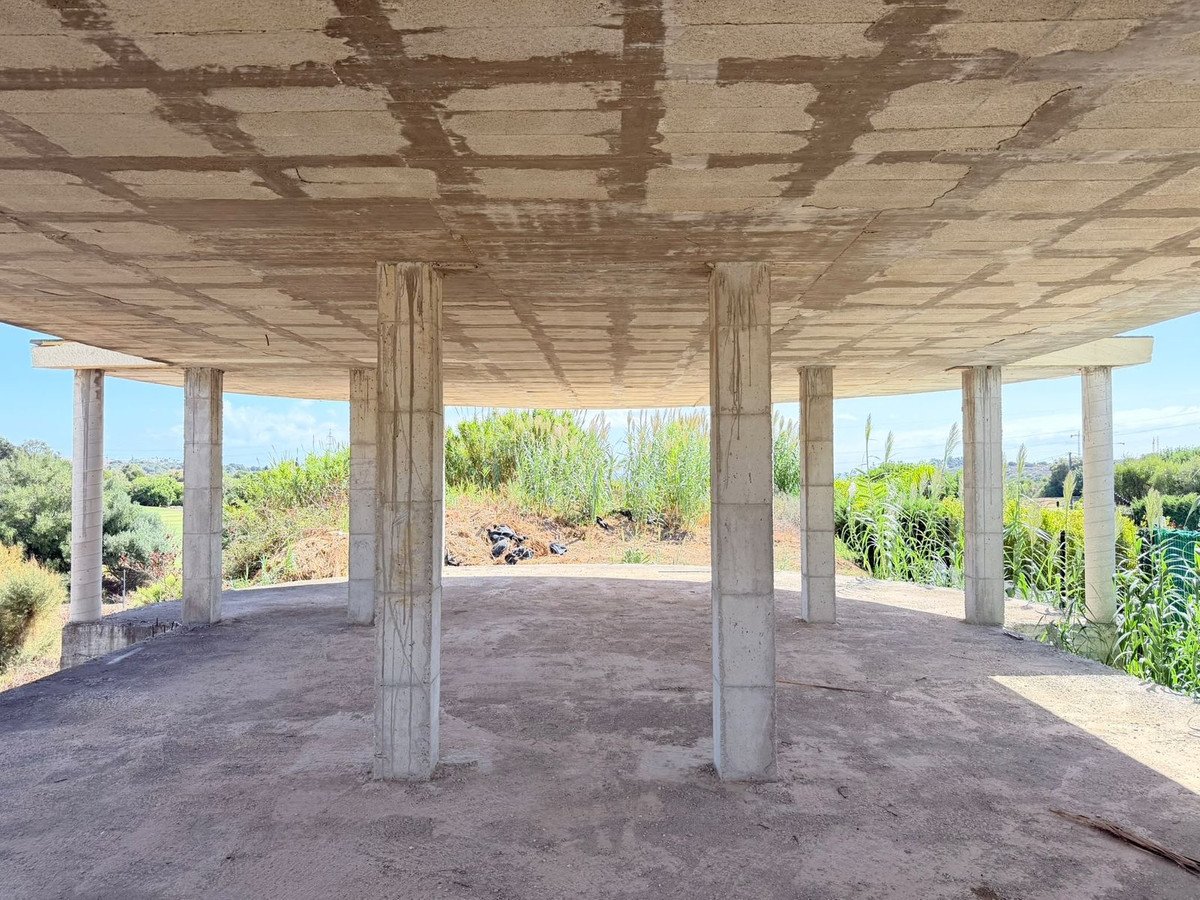 Unfinished concrete structure with columns and an open-air view of greenery under a clear sky.