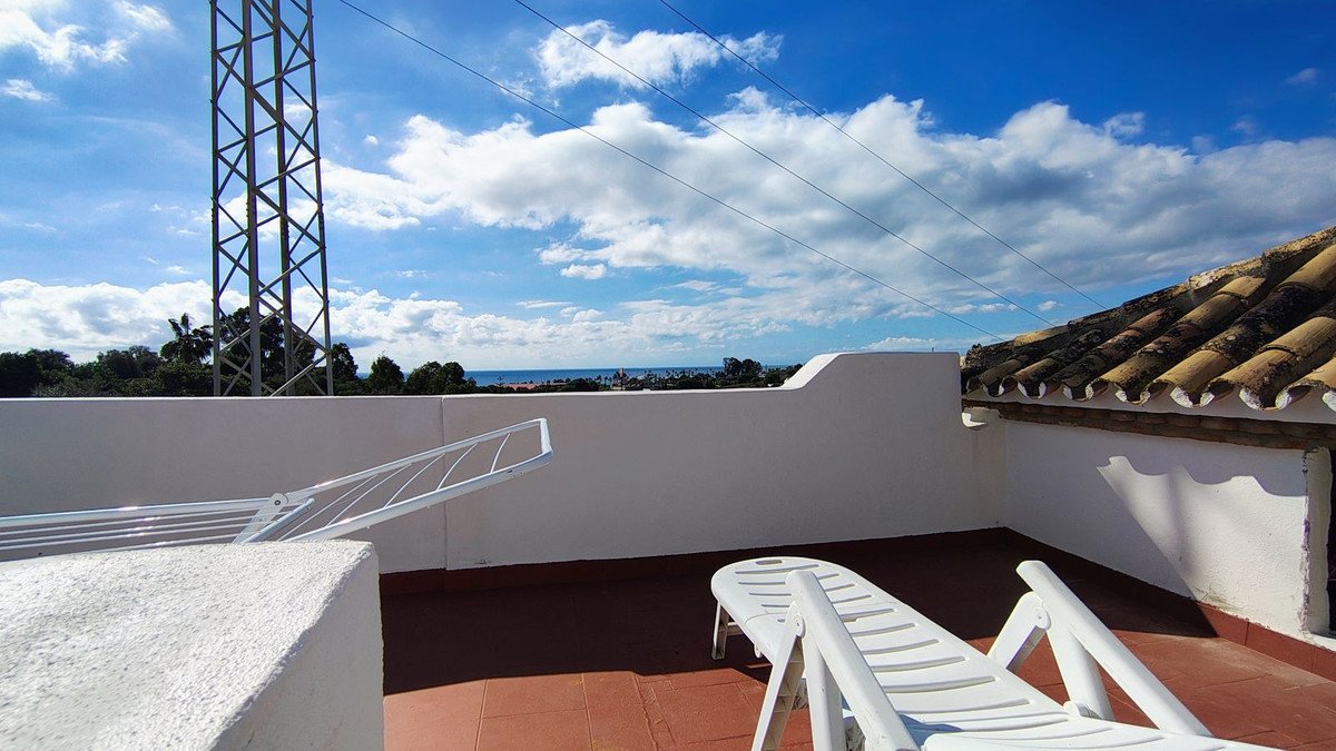 Terrace with sea view, lounge chairs, and a drying rack under a blue sky with clouds.