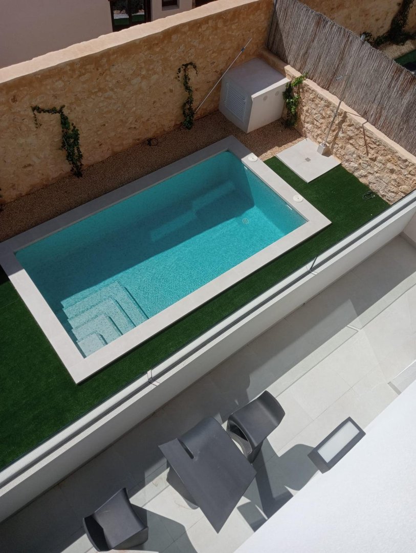 Aerial view of a modern pool with artificial grass, stone walls, and outdoor seating.