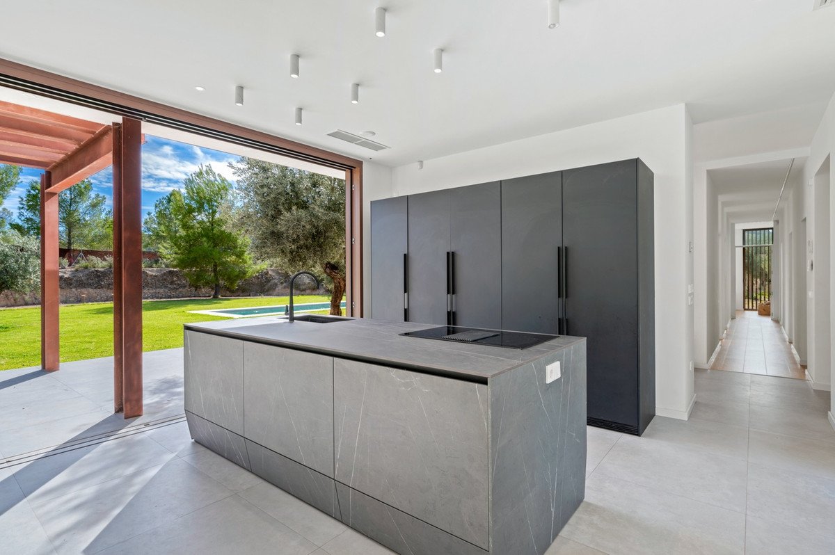 Modern kitchen with gray island, black cabinets, and large glass doors opening to a pool and garden.