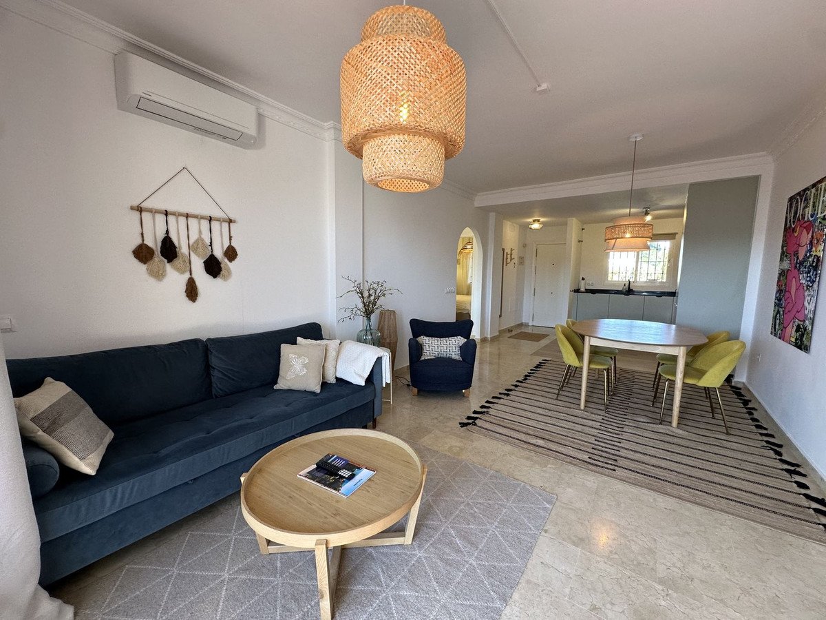Modern living and dining area with a blue sofa, yellow chairs, and a round wooden table, featuring woven pendant lights.