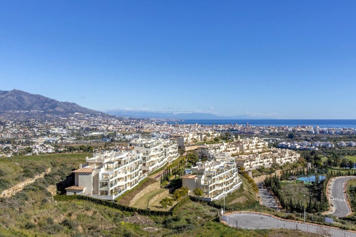 Modern apartment complex with sea and mountain views, terraces, and lush greenery under a clear blue sky.
