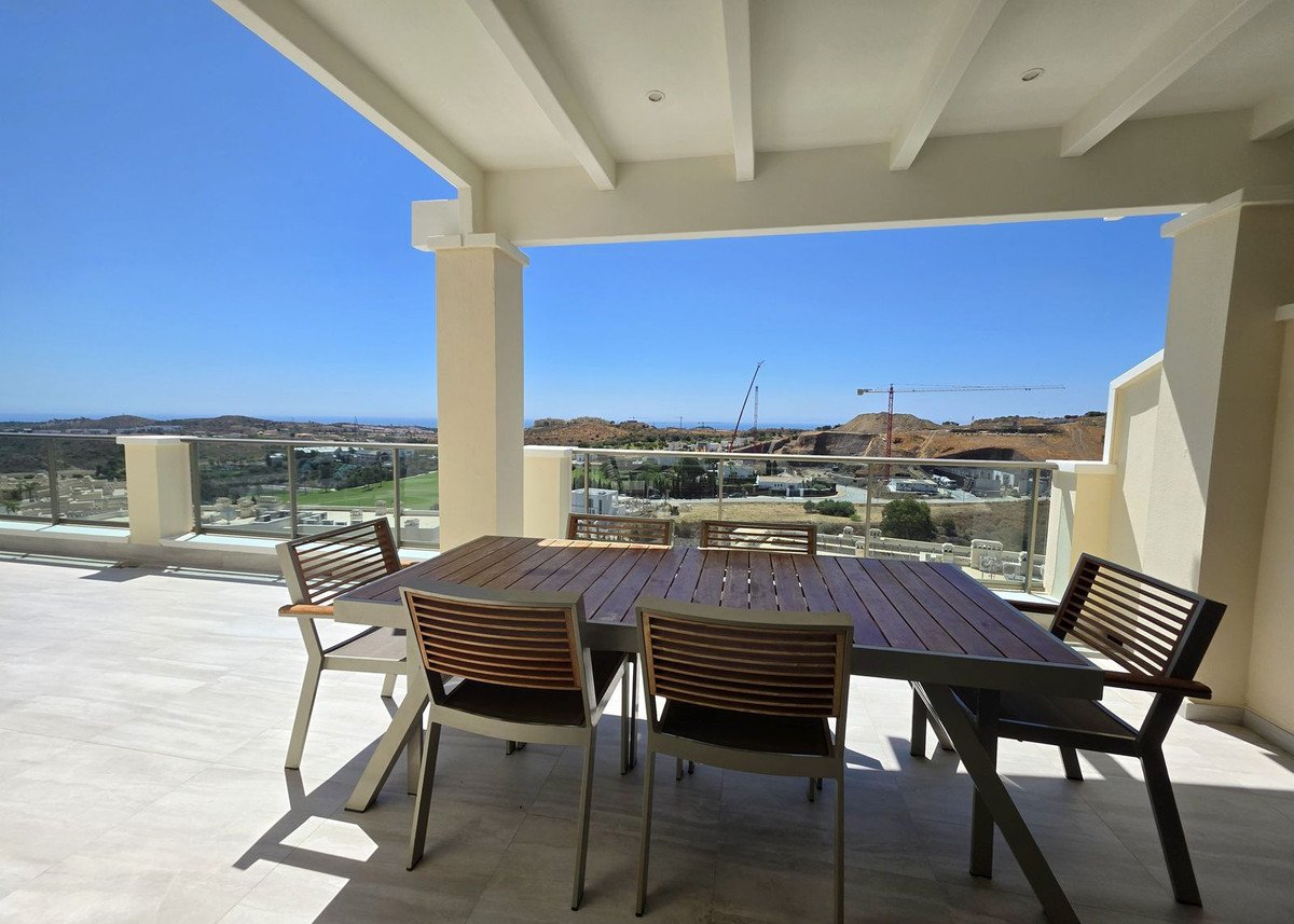 Covered balcony with wooden table and chairs, overlooking a golf course and distant hills under a clear blue sky.
