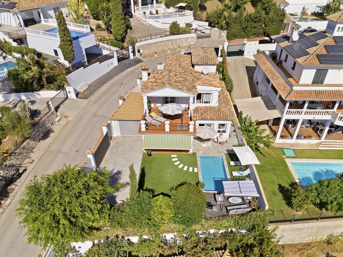 Aerial view of a luxury villa with swimming pools, lush garden, and outdoor seating areas on a sunny day.