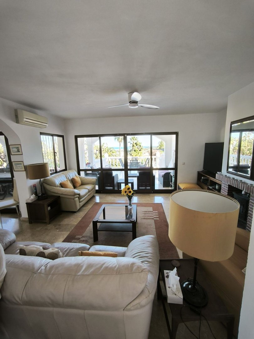 Spacious living room with leather sofas, coffee table, and a view of the patio and sea through large glass doors.