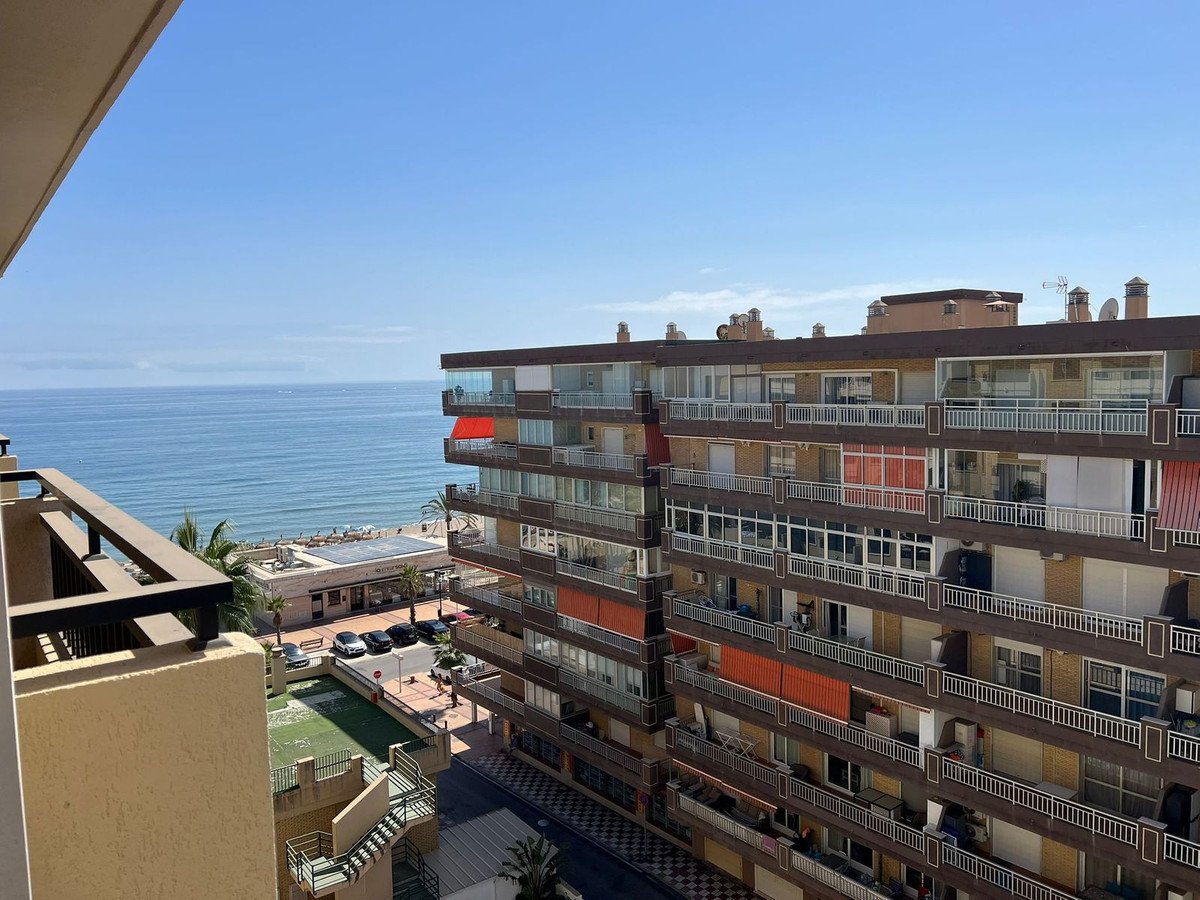 View of the sea and apartments from a balcony, with a swimming pool and parking below.