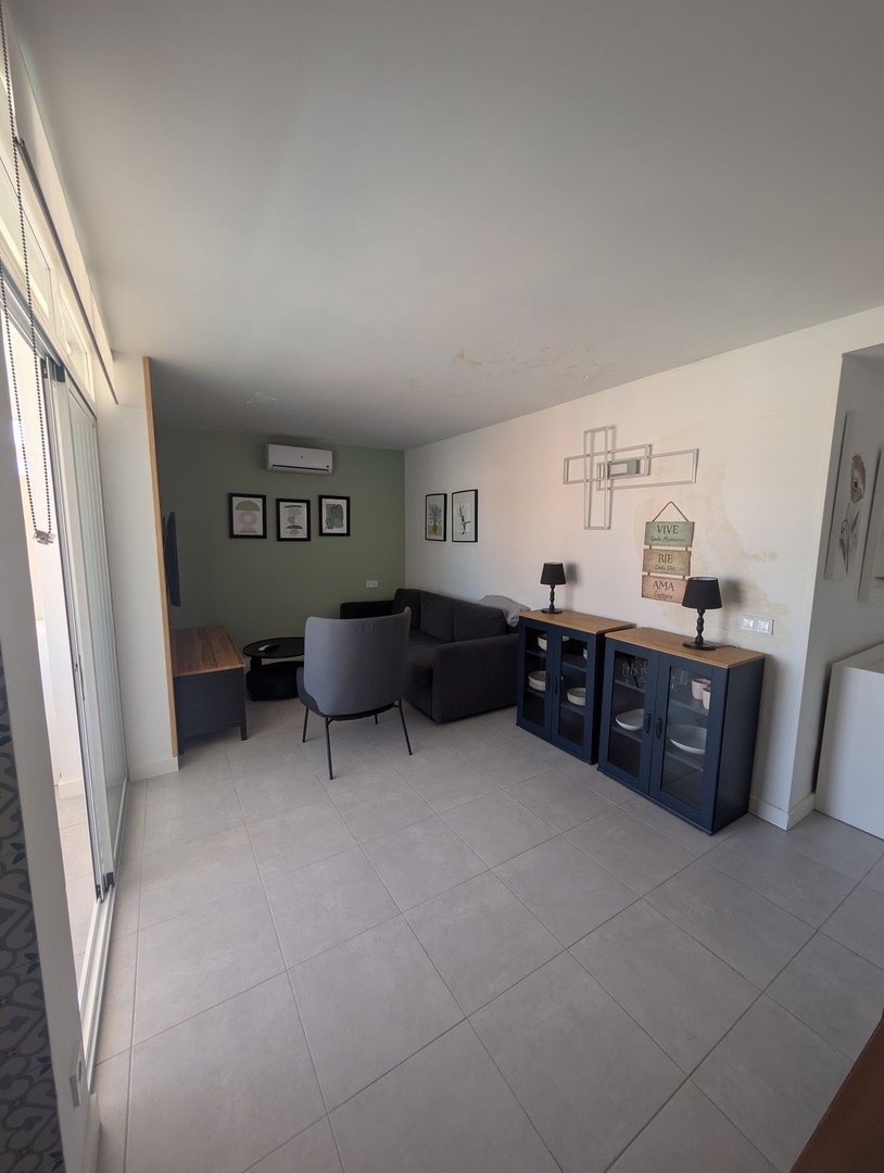 Modern living room with grey sofa, armchair, and cabinets. Features include wall art and air conditioning.