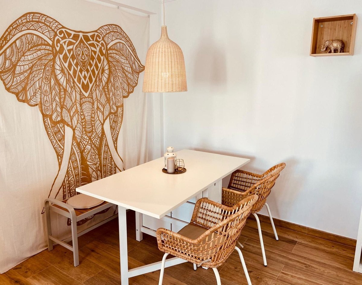 Cozy dining room with white table, wicker chairs, and an elephant tapestry.