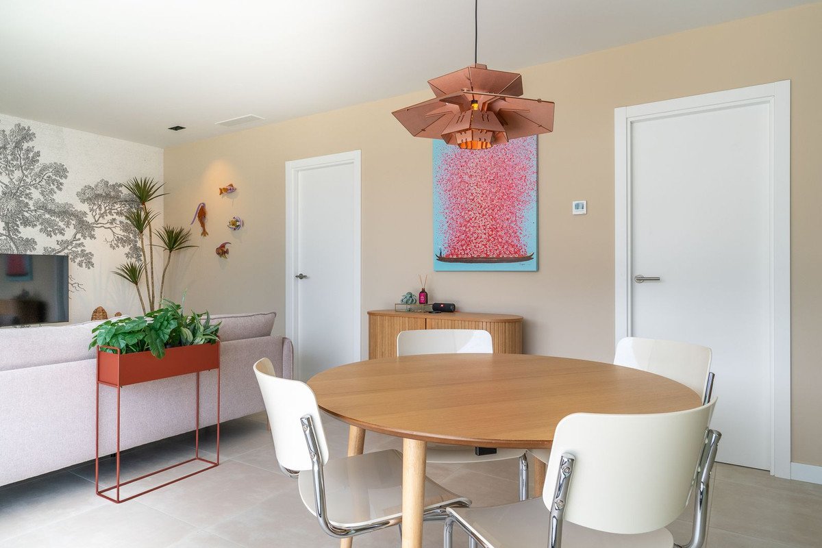 Modern dining and living room with round table, white chairs, and colorful artwork.