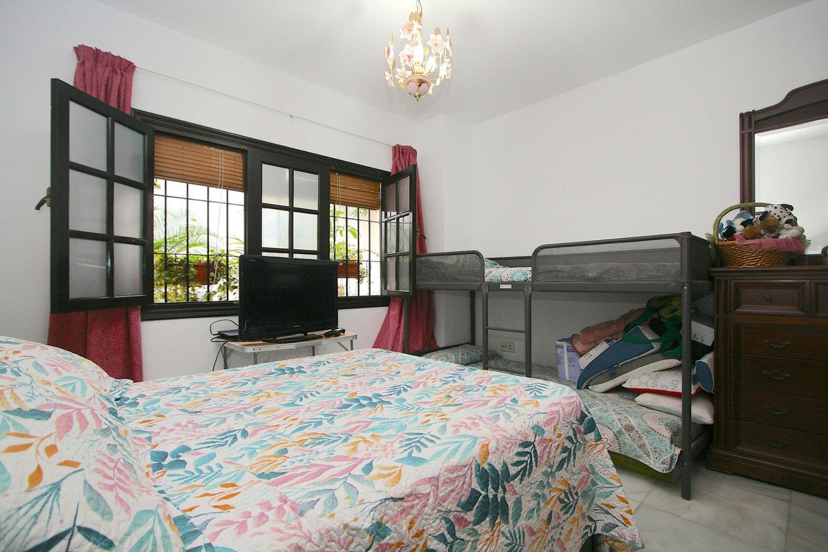 A bedroom with a floral bedspread, bunk beds, a TV, and a window with red curtains overlooking greenery.
