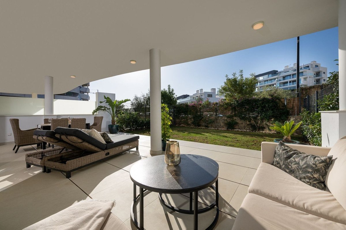 Spacious terrace with outdoor furniture including a sofa, lounge chairs, and dining set, overlooking a garden and modern buildings.