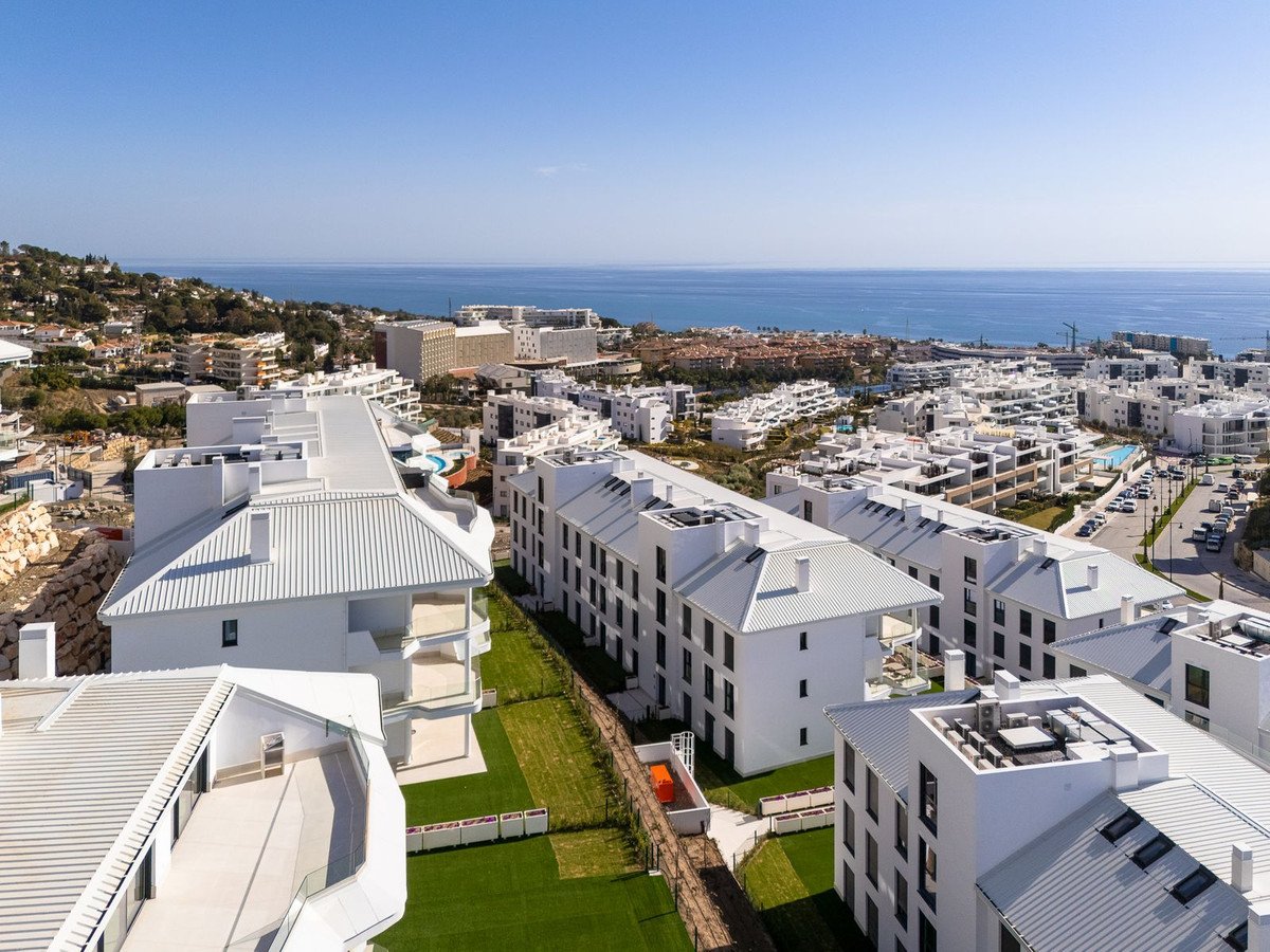Aerial view of modern white apartment buildings with balconies and a distant view of the blue sea under a clear sky.