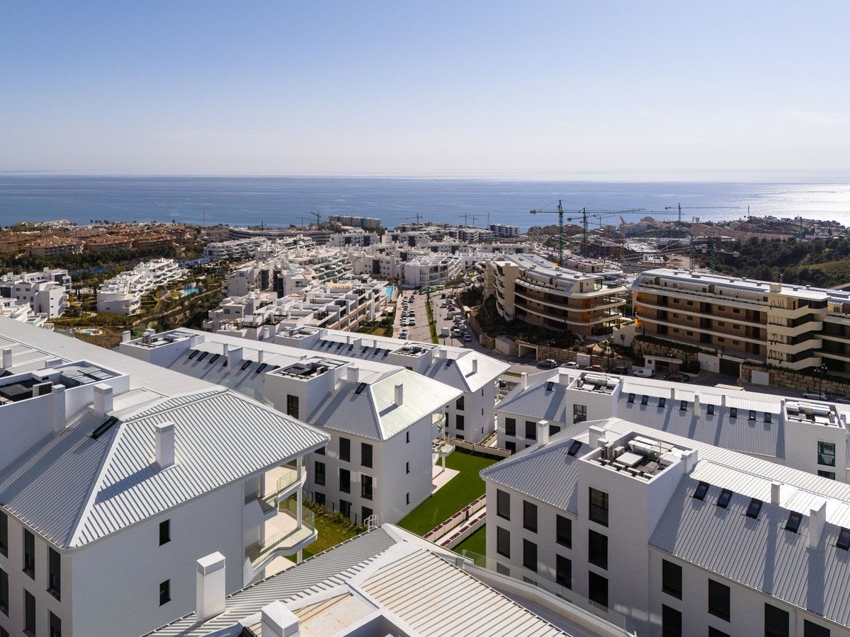 Modern white apartment buildings with balconies and sea view, construction cranes in the distance.