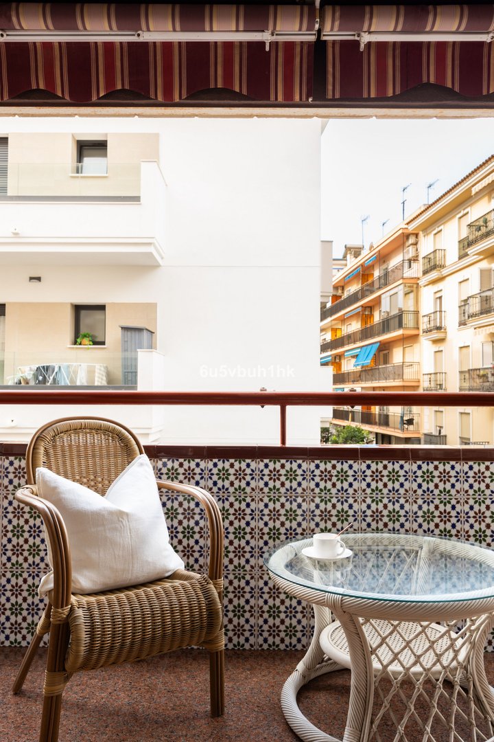 Balcony with wicker chair, glass table, and city view