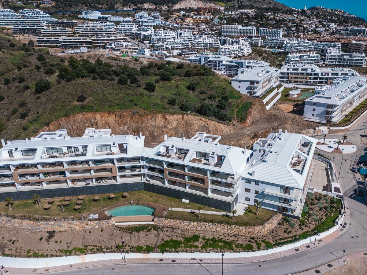 Aerial view of modern apartments with balconies, a swimming pool, and expansive sea and town views.
