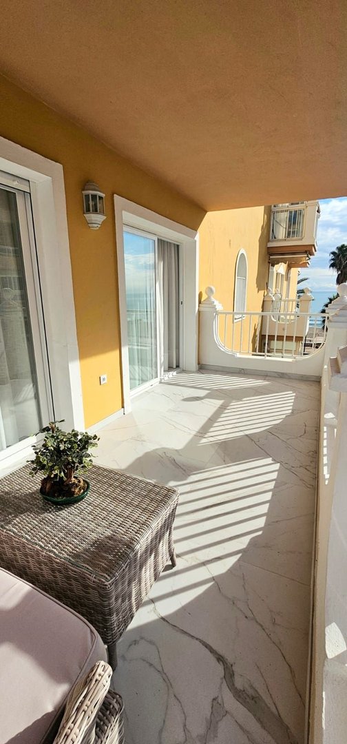 Spacious balcony with sea views, featuring wicker furniture and marble-effect flooring, perfect for outdoor relaxation.