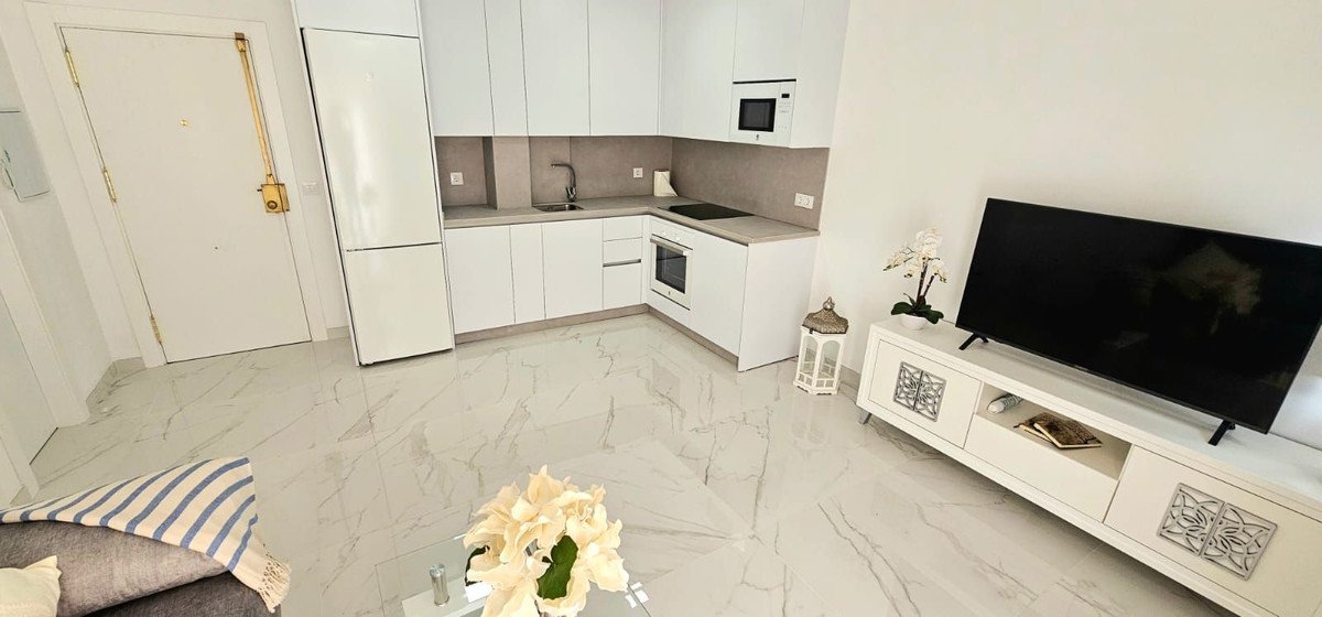 A modern studio apartment with a compact kitchen, living area featuring a TV, and sleek marble flooring.