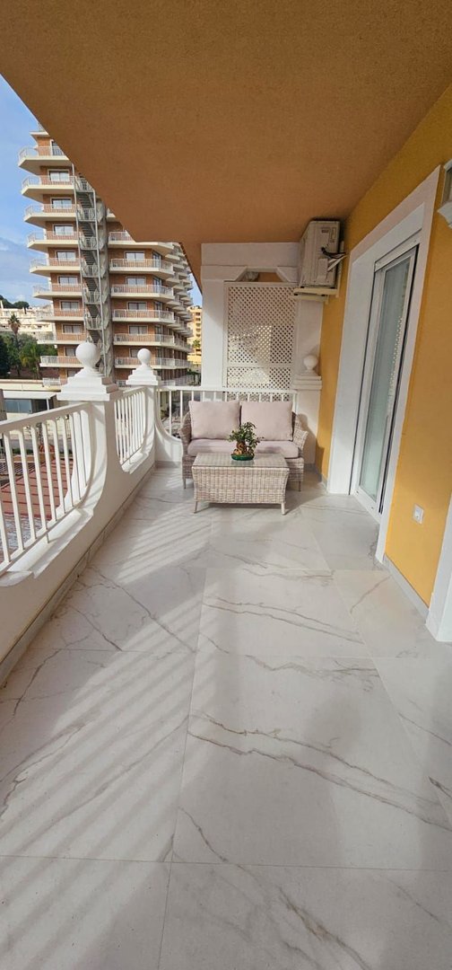 A spacious balcony with white railings, seating furniture, and a view of city buildings.