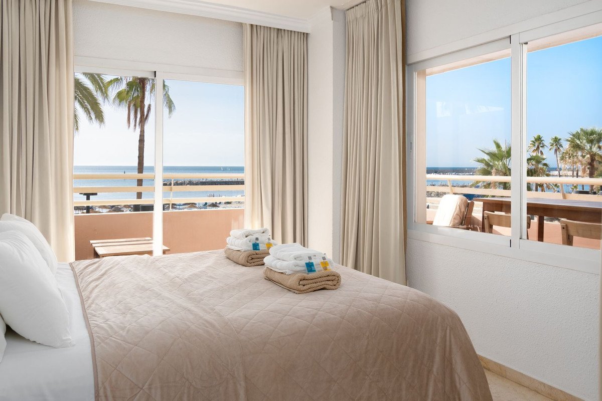 Bedroom with a bed and a balcony overlooking the sea with palm trees.